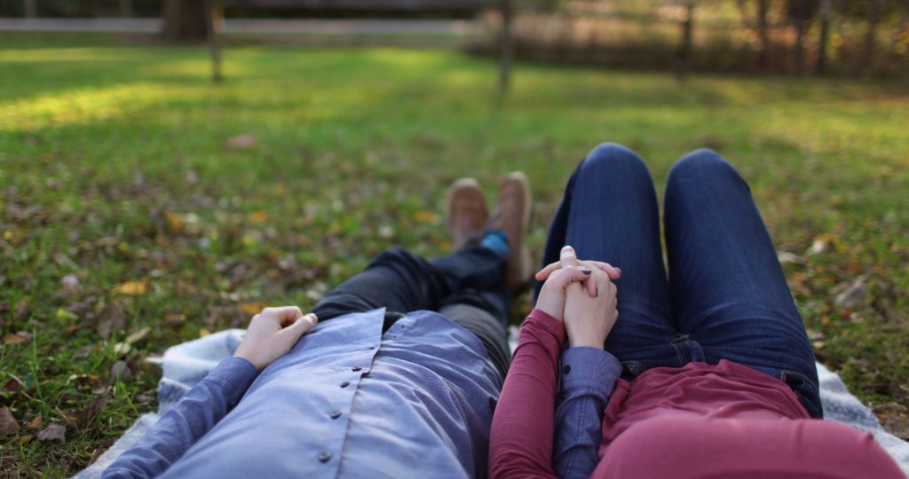 two people laying in grass holding hands
