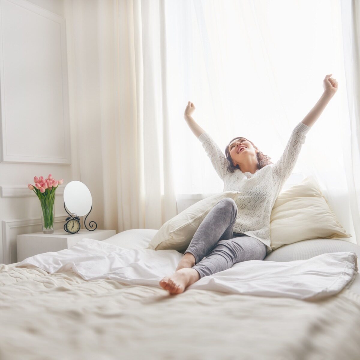 woman on bed with arms in the air happy